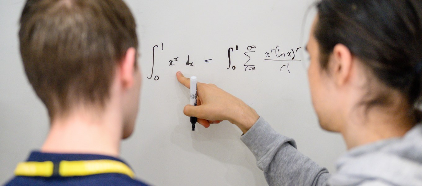 Estudantes discutindo fórmulas matemáticas em frente a um quadro branco